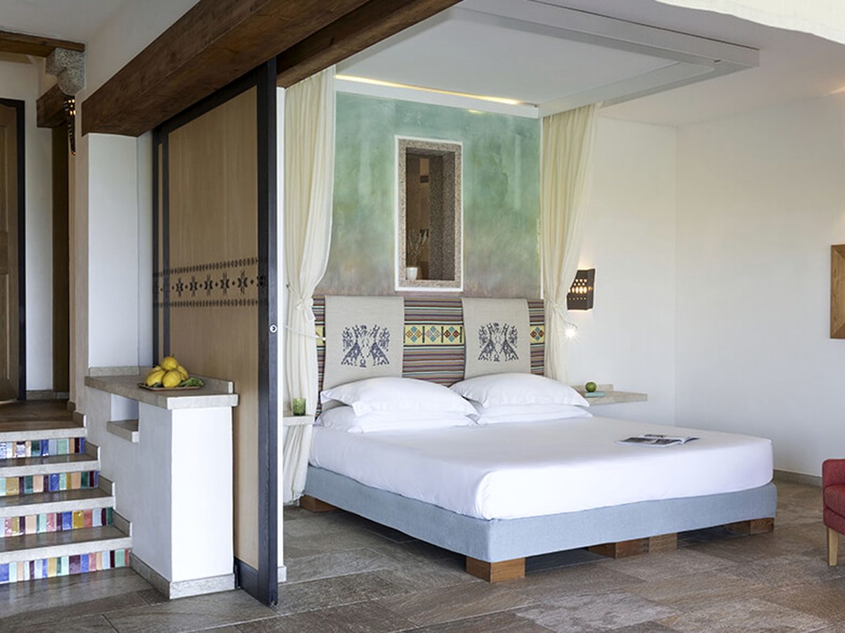 A bedroom with a low double bed and embroidered headboard, a green painted alcove wall and curtains, with tiled steps and a sliding timber door to a lower level on the left.