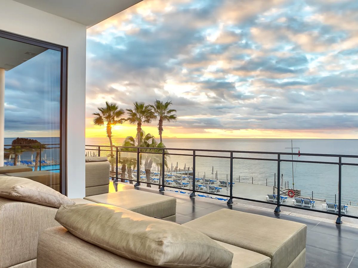 A shaded terrace with cushioned loungers and a low sofa, looking over rows of sun loungers on the deck below and the Atlantic beyond.