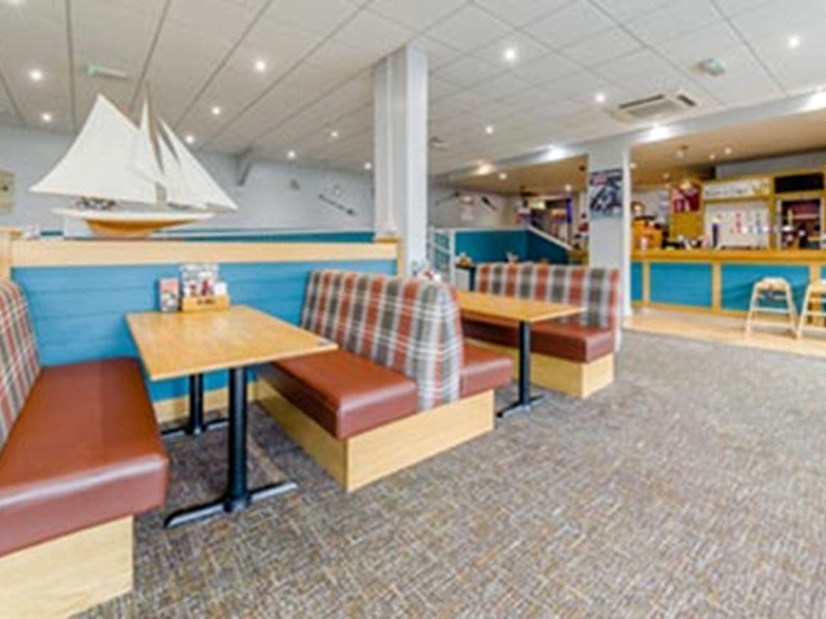 The inside of the bar and restaurant, with tan leather and tartan booth seating, pale timber tables, blue panelled walls, a model sailing yacht on a shelf and the bar counter beyond.