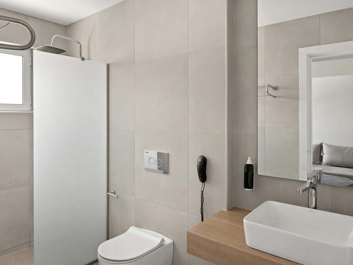 Bathroom with a walk-in rainfall shower behind a white screen, a wall-hung toilet, a rectangular basin on a wooden shelf and a large mirror.