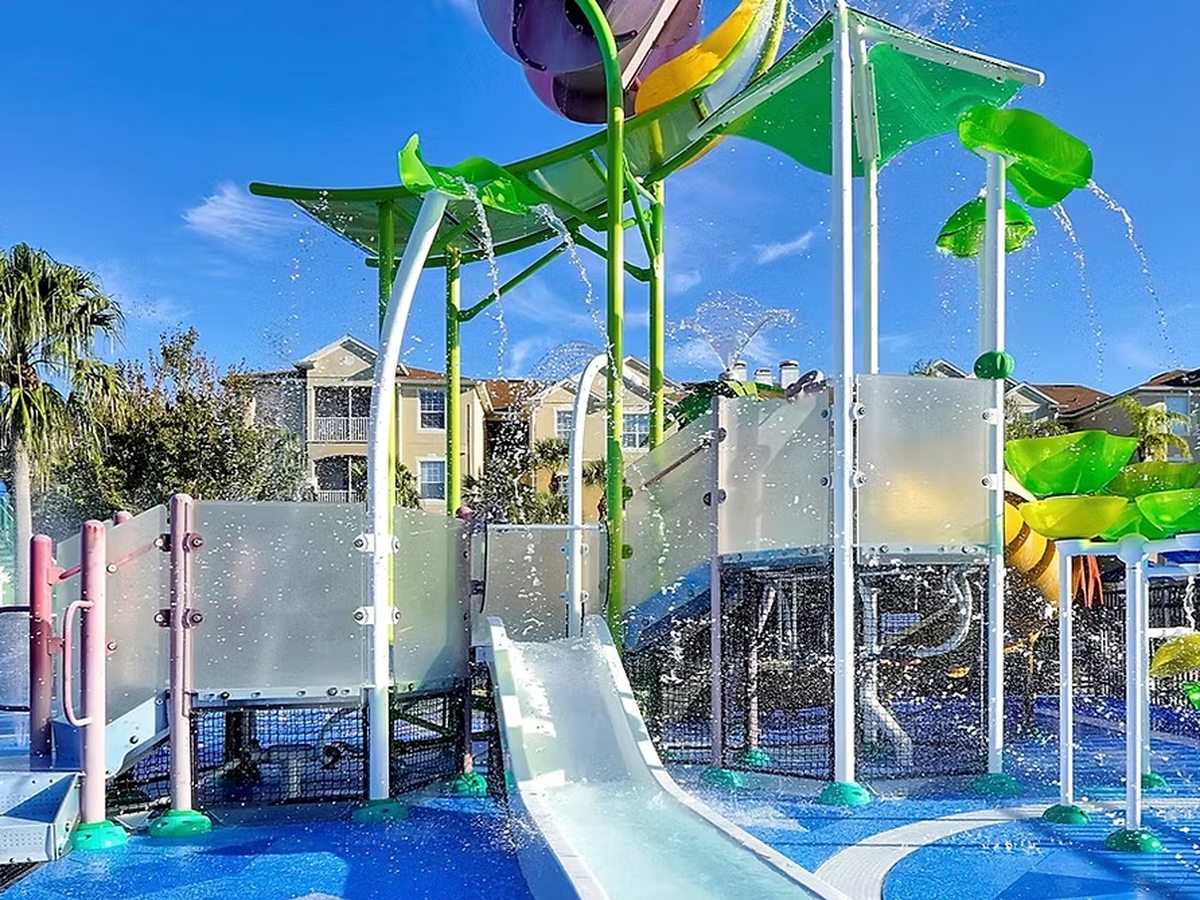 A tall multi-level metal water-play structure with green and yellow slides and spray features against a clear blue sky.