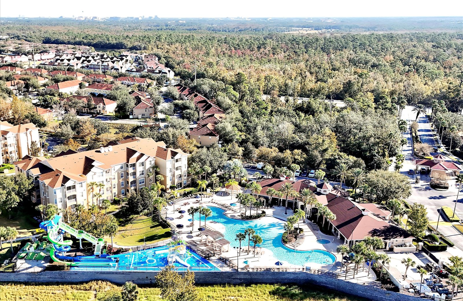 Windsor Hills Resort from the air: a gated community of low-rise buildings and villas set among trees, with a curved blue lagoon pool and a colourful water park at its centre.