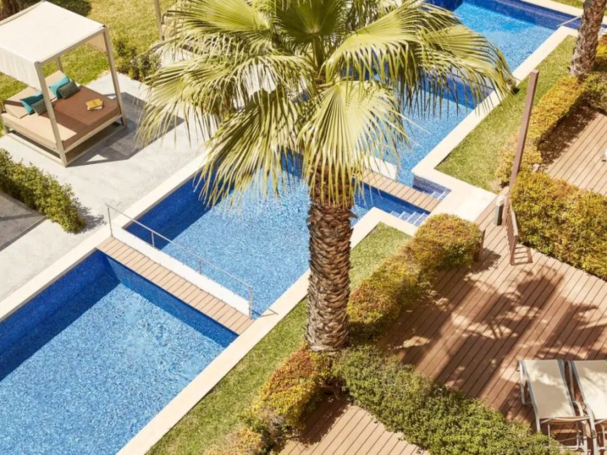 Looking down on three small rectangular pools separated by lawn and decking, with a canopied daybed and a palm tree between them.
